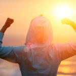 Back view of strong motivated woman celebrating workout goals towards the sun. Morning healthy training success.