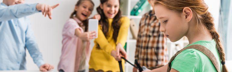 panoramic shot of schoolkids bullying schoolgirl in classroom