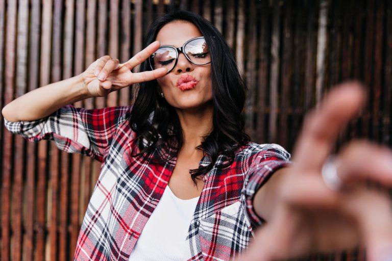 Romantic girl posing on wooden background in sparkle glasses. Fashionable lady making selfie with e