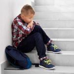 Little school boy sitting alone on stairs on school.