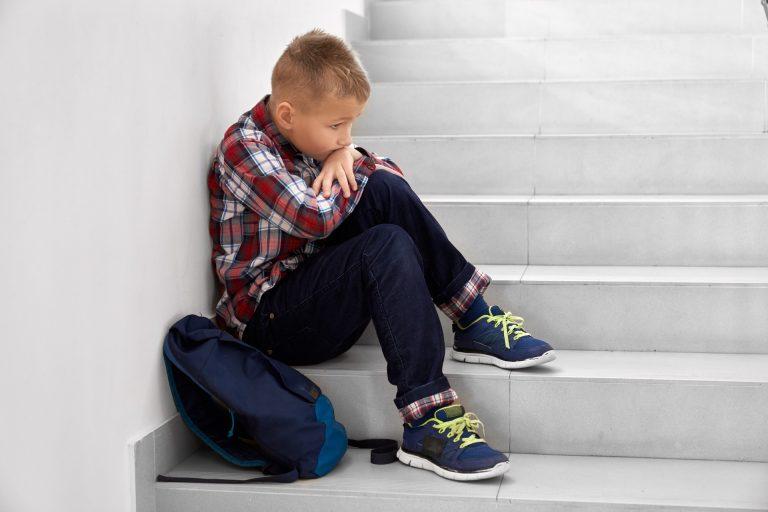 Little school boy sitting alone on stairs on school.