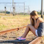 Upset teenager girl sitting on rail track in countryside