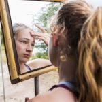 Botswana,Thirteen year old girl looking into mirror at a tented camp, applying sunscreen to her forehead