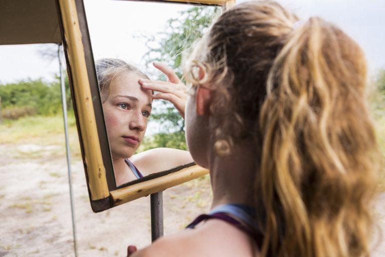 Botswana,Thirteen year old girl looking into mirror at a tented camp, applying sunscreen to her forehead