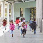 Elementary school kids run from camera in school corridor